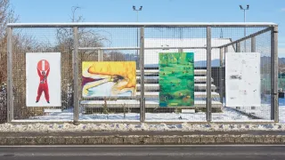 Three colorful paintings are displayed on a metal fence against a snowy background with a blue sky.