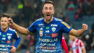 A soccer player celebrates with arms outstretched in a blue jersey with various sponsors' logos.