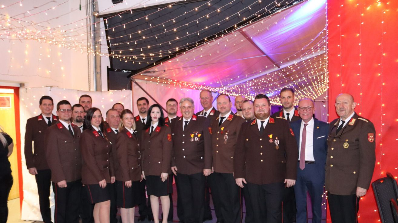 Eine Gruppe uniformierter Personen steht in einem festlichen Ambiente, geschmückt mit Medaillen und Lächeln, unter einer mit Lichtern dekorierten Decke.