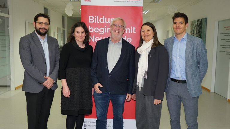 Five people are standing in front of a red banner that says Bildung beginnt mit Neugierde. They are smiling for the camera.