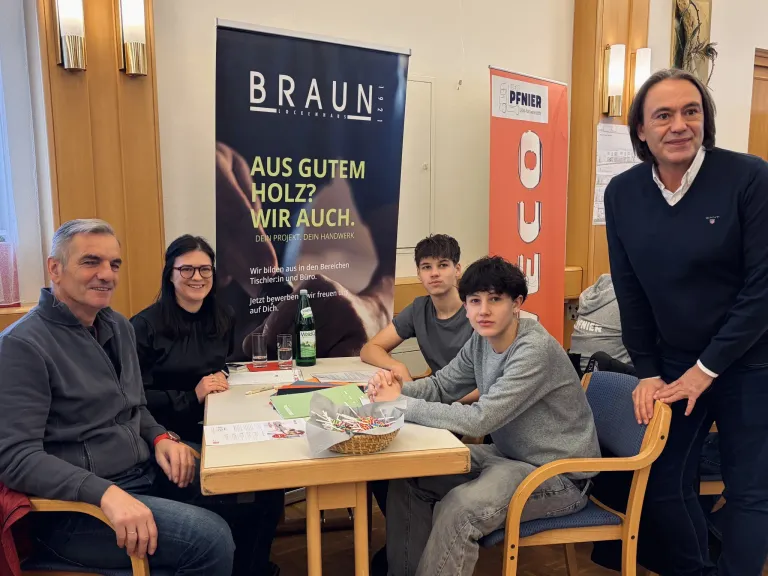 Eine Gruppe von Menschen sitzt um einen Tisch herum, vor ihnen ein Banner, das für Braun Lockenhaus wirbt. Ein Mann und eine Frau lächeln und posieren für ein Foto.