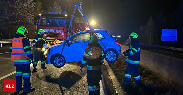 Rettungskräfte in Uniform stehen neben einem beschädigten Auto bei Nacht, mit einem Feuerwehrwagen in der Nähe. Das Auto wird von einem Kran angehoben.