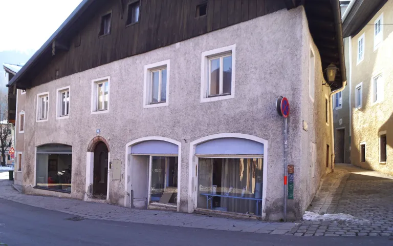 Ein dreistöckiges Gebäude mit mehreren Fenstern und zwei Geschäften im Erdgeschoss. Ein Parkverbotsschild befindet sich auf der rechten Seite.