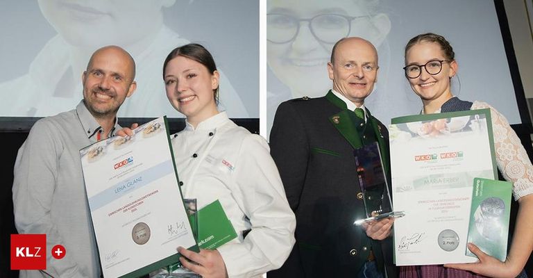 A smiling chef holds a certificate, while another holds a trophy. Behind them, a man in a green jacket and a woman in glasses smile. Behind the man, a picture of a smiling woman is displayed.