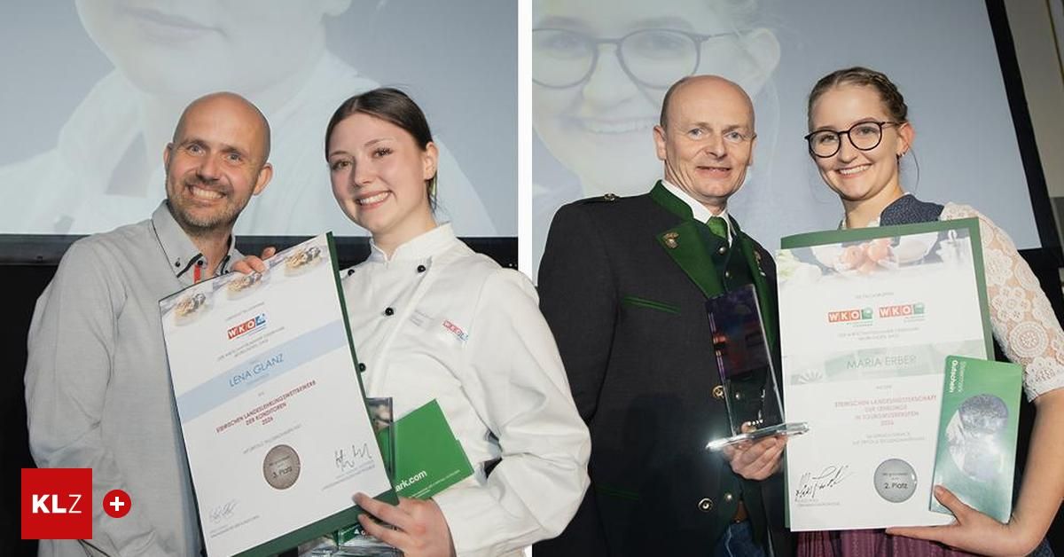 A smiling chef holds a certificate, while another holds a trophy. Behind them, a man in a green jacket and a woman in glasses smile. Behind the man, a picture of a smiling woman is displayed.