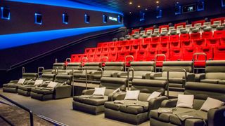An empty luxury movie theater with red and gray seating, blue lighting, and a sign reading 'Deluxe'.