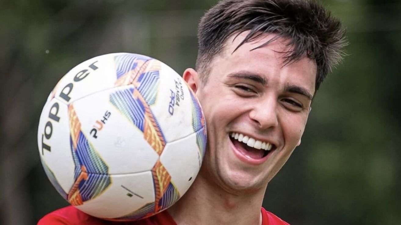 A soccer player is holding a soccer ball in his hands. He is smiling and posing for a picture.