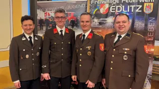 Vier Männer in Militäruniformen stehen nebeneinander vor Bannern. Der Mann auf der linken Seite lächelt.