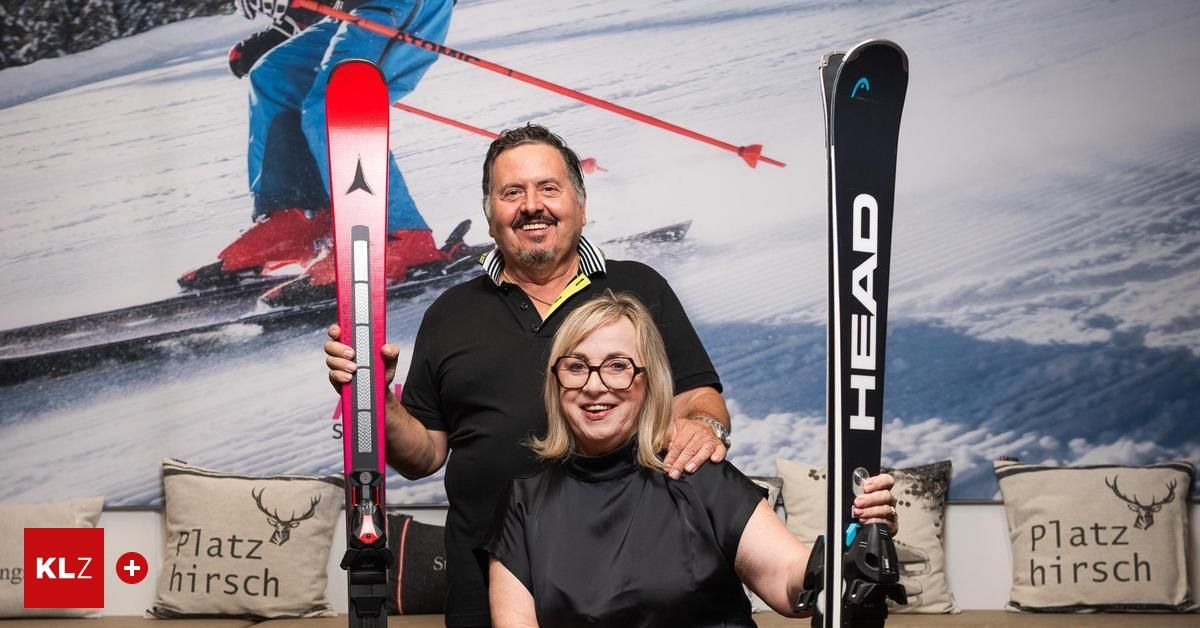 Ein Mann und eine Frau stehen nebeneinander und halten Skier. Der Mann trägt ein schwarzes Poloshirt, und die Frau trägt ein schwarzes Kleid. Sie lächeln und scheinen für ein Foto zu posieren.