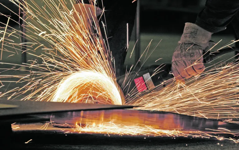 Eine Nahaufnahme eines Metallschneideprozesses mit fliegenden Funken. Ein kreisförmiges Blatt schneidet durch ein Metallblech und produziert helle Funken.