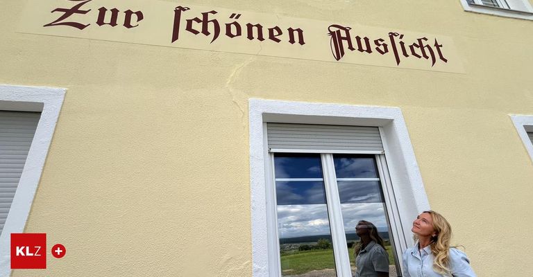 Eine Frau schaut aus einem Fenster eines Gebäudes mit einem Schild, das 'Wer Schonen Ausflieb' steht. Das Fenster zeigt die Reflexion einer anderen Frau und eines grünen Feldes.