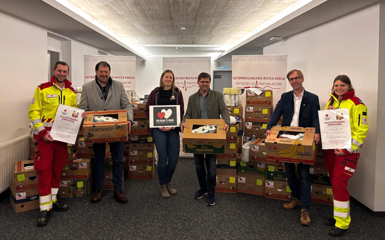 Vier Personen stehen vor einer großen Menge Bananen. Drei Männer und eine Frau. Alle lächeln und schauen in die Kamera.