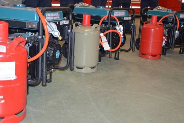 Mehrere Gasgeneratoren mit roten und grauen Tanks sind in einer Reihe aufgestellt und durch orangefarbene Schläuche verbunden, in einem Lagerhaus.