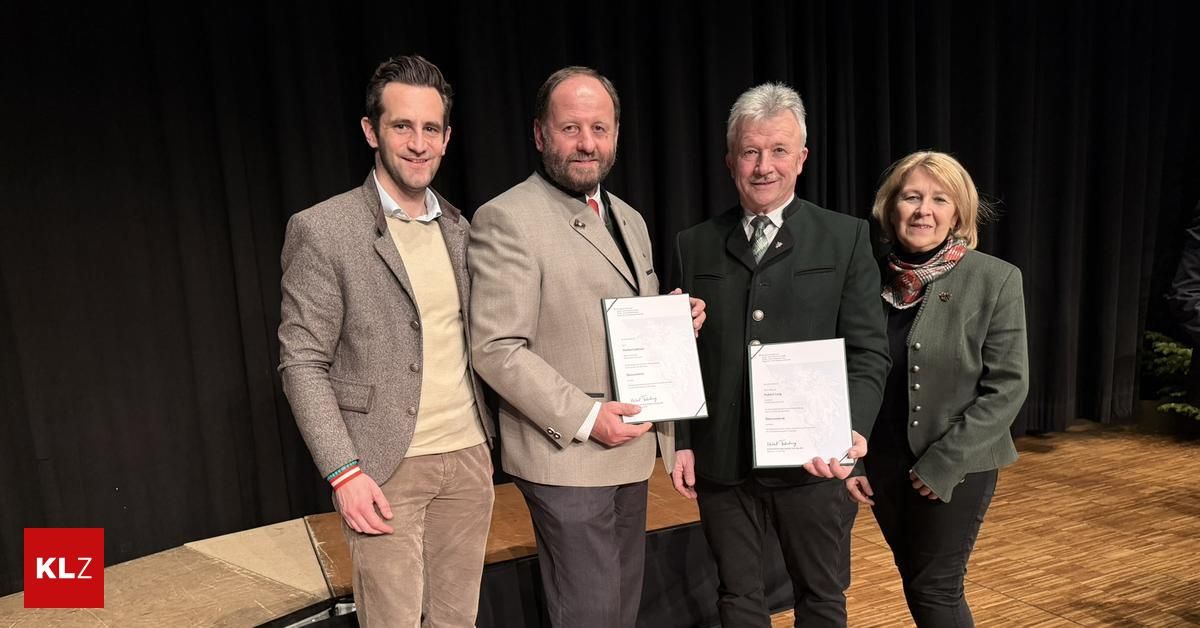 Vier Menschen stehen lächelnd auf einer Bühne und halten Urkunden. Der Mann in der Mitte hält zwei Urkunden. Hinter ihnen ist ein schwarzer Vorhang.
