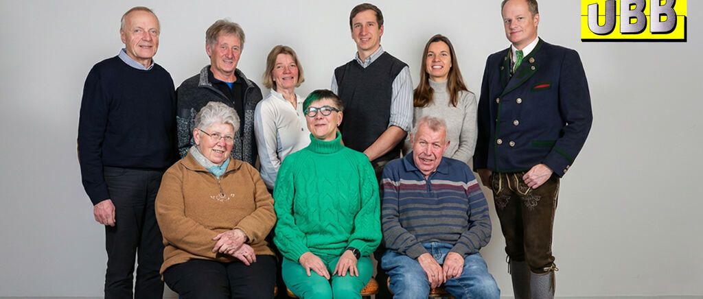 Eine Gruppe von Menschen steht und sitzt, lächelt und posiert für ein Foto. Sie tragen verschiedene Kleidungsstücke und Accessoires.