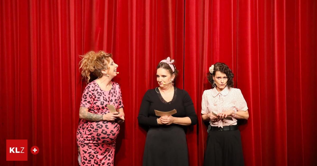 Drei Frauen stehen auf einer Bühne, halten Papiere und haben einen roten Vorhang im Hintergrund. Die Frau auf der linken Seite lächelt und hält ein Mikrofon. Die mittlere Frau hält ein Papier mit einem Mikrofon. Die Frau auf der rechten Seite sieht ernst aus und hält ein Papier.