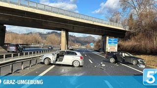 Zwei Autos sind auf einer Autobahn mit einer Überführung darüber beschädigt. Die Autos befinden sich auf gegenüberliegenden Seiten, und Trümmerteile sind auf der Straße verstreut. Ein Schild befindet sich rechts, und ein Berg ist im Hintergrund.