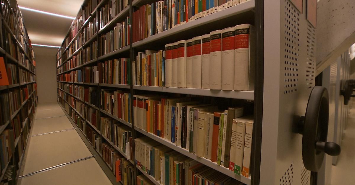 Reihen von Bücherregalen gefüllt mit verschiedenen Büchern in unterschiedlichen Größen und Farben. Die oberste Reihe besteht aus einer Reihe weißer Bücher mit roten und schwarzen Rücken.