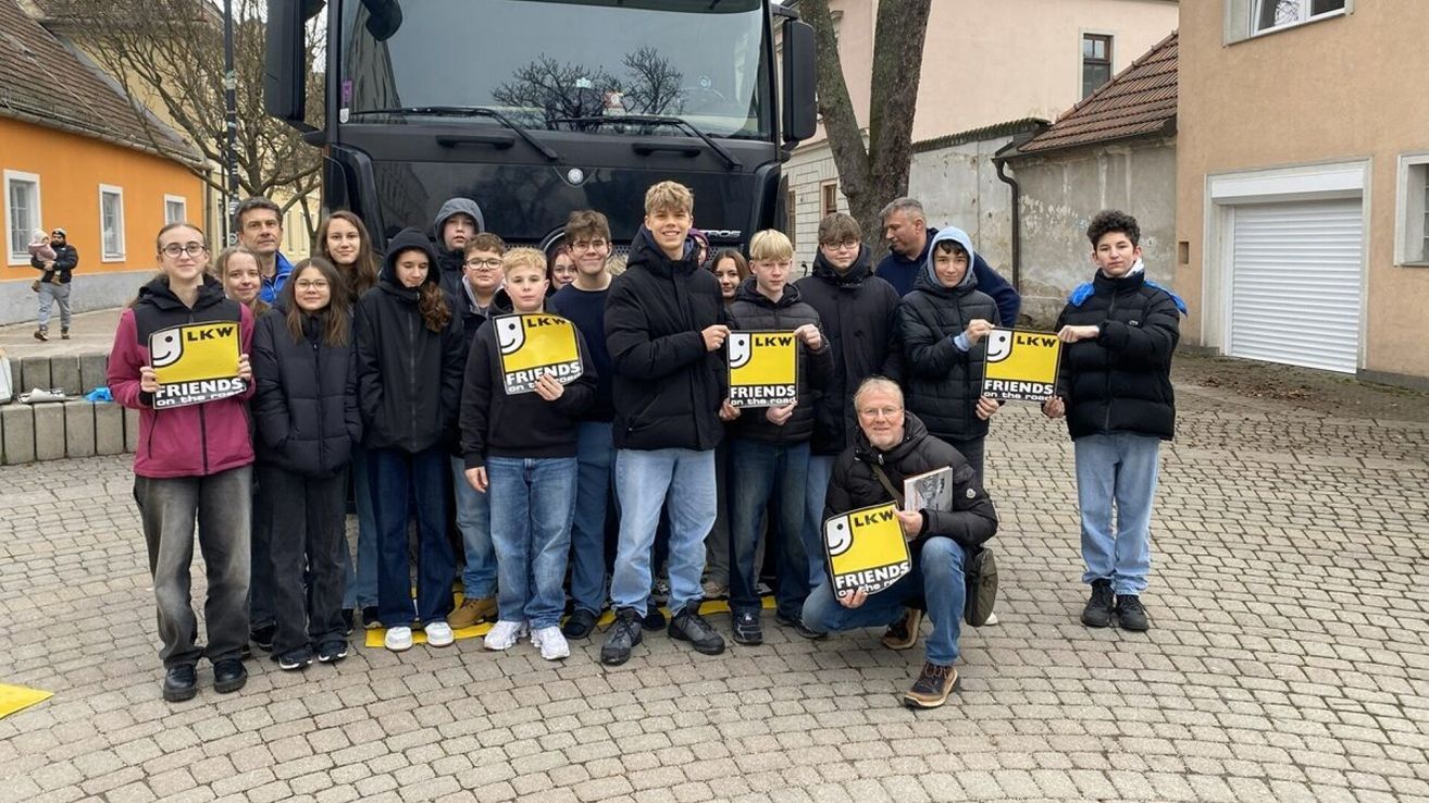 Eine Gruppe von Menschen in Winterkleidung steht vor einem Bus. Sie halten Schilder mit der Aufschrift 'Freunde auf der Straße'.