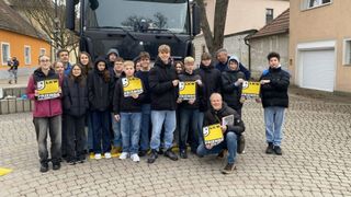 Eine Gruppe von Menschen in Winterkleidung steht vor einem Bus. Sie halten Schilder mit der Aufschrift 'Freunde auf der Straße'.