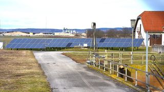 Ein Solarkraftwerk mit vielen Solarmodulen auf einem Feld, mit einem Weg, der zu einem Pumpen- und Rohrleitungssystem führt.