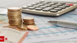 Stapel von Münzen neben einem Taschenrechner und einem Stift auf einem Finanzdokument mit Zahlen und Prozentsätzen.