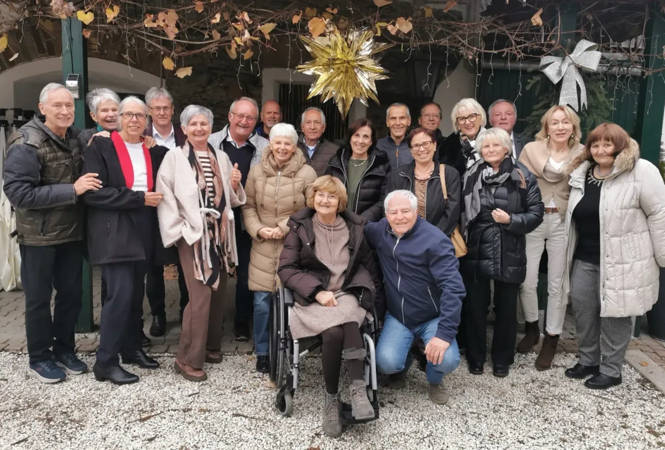 Eine Gruppe von Menschen, darunter einige im Rollstuhl, posiert für ein Foto im Freien und trägt Winterkleidung. Ein goldener Stern hängt über ihnen.