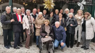 Eine Gruppe von Menschen, darunter einige im Rollstuhl, posiert für ein Foto im Freien und trägt Winterkleidung. Ein goldener Stern hängt über ihnen.