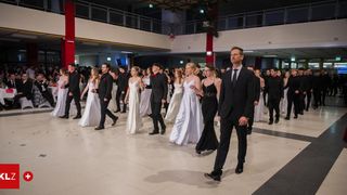 Eine Gruppe formell gekleideter Menschen geht gemeinsam in einem großen Raum, möglicherweise bei einer Veranstaltung.