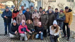 Eine Gruppe von Menschen in Winterkleidung posiert mit einem Hund vor einem Gebäude mit Bäumen.