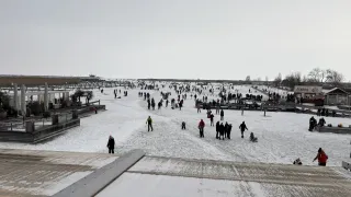 Eine Luftaufnahme eines verschneiten Feldes mit vielen Menschen. Einige stehen, andere gehen. Bäume und Gebäude sind in der Ferne sichtbar.