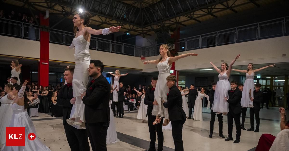 Eine Gruppe von Menschen in weißen Kleidern führt Akrobatik auf den Köpfen ihrer männlichen Gegenstücke in einem Saal auf.