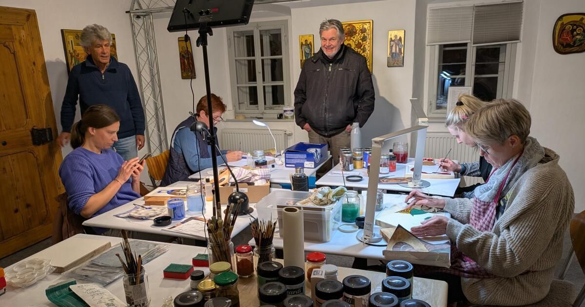 Eine Gruppe von Menschen arbeitet an Kunstprojekten. Sie sitzen um einen Tisch mit Kunstmaterialien herum. Ein Mann steht hinter ihnen und eine Frau rechts malt.