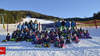 Eine Gruppe von Kindern und Erwachsenen posiert für ein Foto auf einem verschneiten Hang, mit einem Banner im Hintergrund.