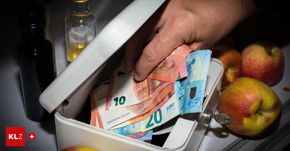 Eine Hand nimmt einen 20-Euro-Schein aus einer Box, die mit verschiedenen Euro-Scheinen und einer Flasche Öl gefüllt ist.