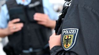 Zwei Polizeibeamte in schwarzen Uniformen. Einer hat eine verschwommene Hand, die ein Gerät hält.