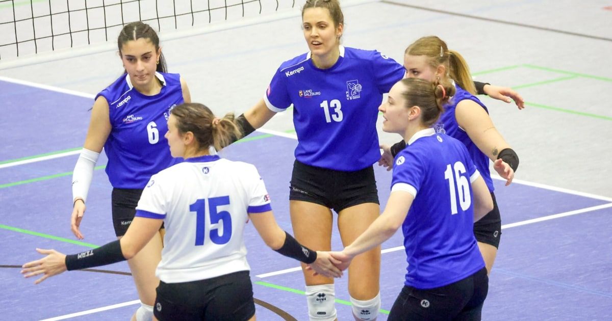 Fünf Frauen in blauen und weißen Volleyballtrikots stehen auf einem Spielfeld. Eine Frau trägt ein blaues Trikot mit der Nummer 13 und umarmt eine andere Spielerin. Die anderen drei Spielerinnen schauen zu ihnen.