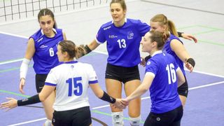 Fünf Frauen in blauen und weißen Volleyballtrikots stehen auf einem Spielfeld. Eine Frau trägt ein blaues Trikot mit der Nummer 13 und umarmt eine andere Spielerin. Die anderen drei Spielerinnen schauen zu ihnen.