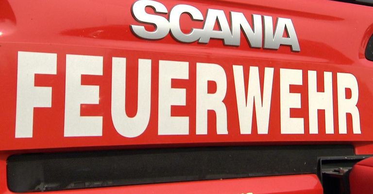 Ein rotes Schild mit weißen Buchstaben, die 'SCANIA' und 'FEUERWEHR' lesen, ist auf einem roten Hintergrund angebracht. Die Buchstaben sind groß und fett, und das Schild ist wahrscheinlich an einem Fahrzeug befestigt.