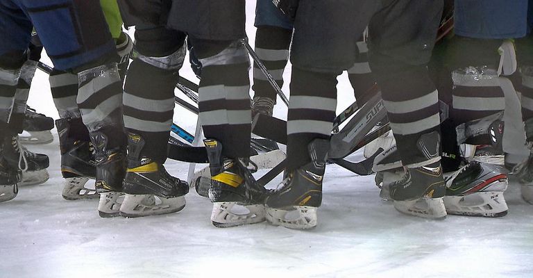 Eine Gruppe von Hockeyspielern in schwarzen und grauen Uniformen und Schlittschuhen versammelt sich auf einer Eisbahn.