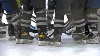 Eine Gruppe von Hockeyspielern in schwarzen und grauen Uniformen und Schlittschuhen versammelt sich auf einer Eisbahn.
