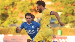Zwei Fußballspieler in blauen und gelben Trikots laufen auf einem Feld mit unscharfem Hintergrund. Der Spieler in Blau schaut den Spieler in Gelb an.