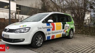 Ein weißer Minivan ist vor einem Gebäude geparkt, mit dem Text 'Das Sammeltaxi in der Oststeiermark' und einer Comicfigur an der Seite.