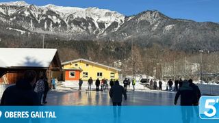 Eine Gruppe von Menschen Schlittschuh fährt auf einer Eisbahn in einem verschneiten Gebirgsgebiet mit einem gelben Gebäude hinter ihnen.