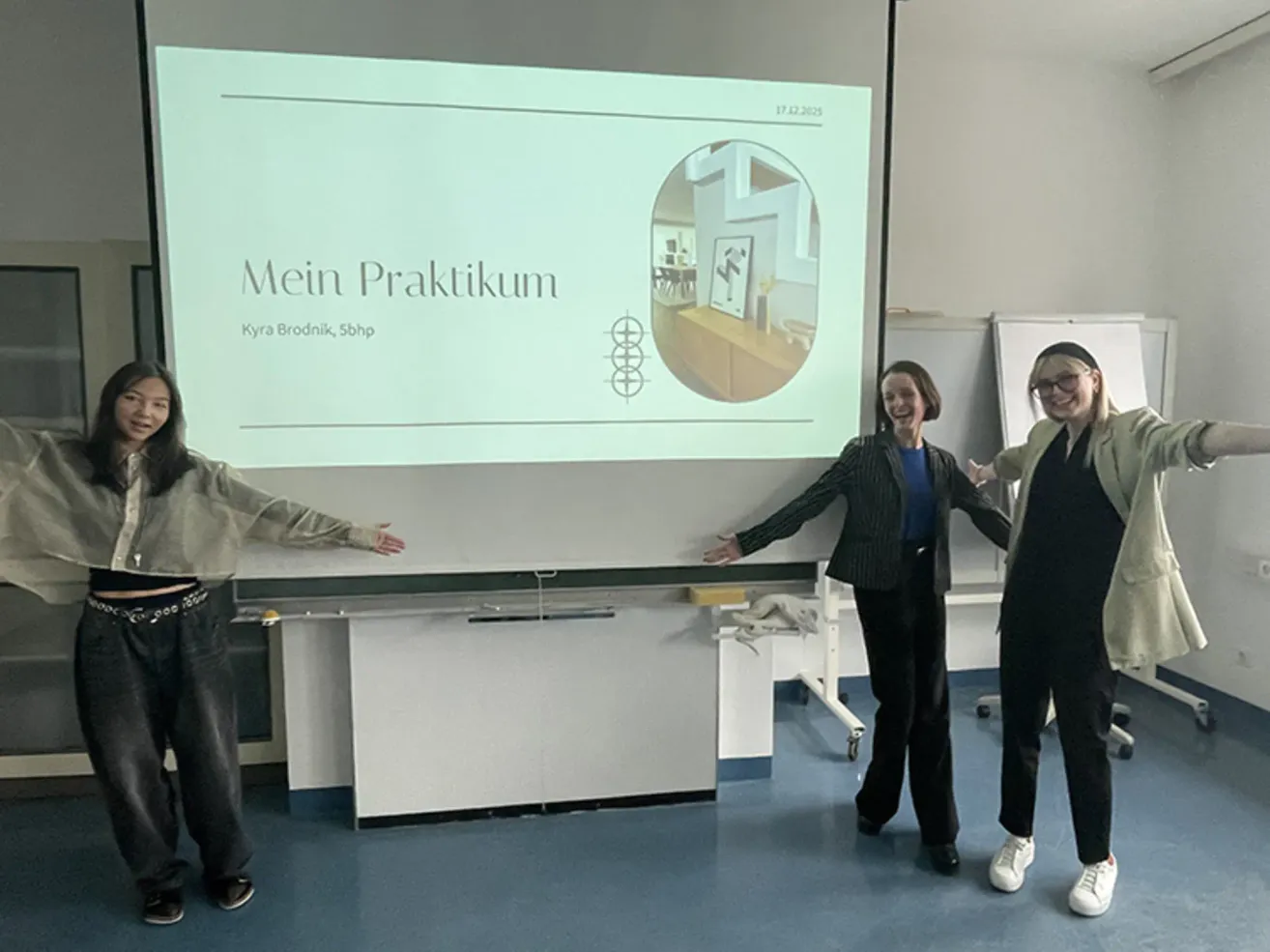 Drei Frauen stehen vor einer Projektionsleinwand mit einer Präsentation mit dem Titel 'Mein Praktikum' von Kyra Brodnik. Die Frau auf der linken Seite lächelt, während die anderen beiden lachen. Dahinter steht eine Tafel und ein Tisch.