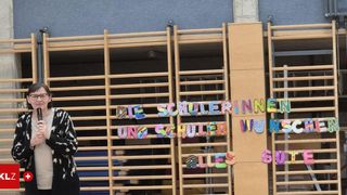 Ein Holzzaun mit bunter Schrift, die 'Die Schulerinnen und Schuler Wuns alles gut' sagt. Eine Person steht links.