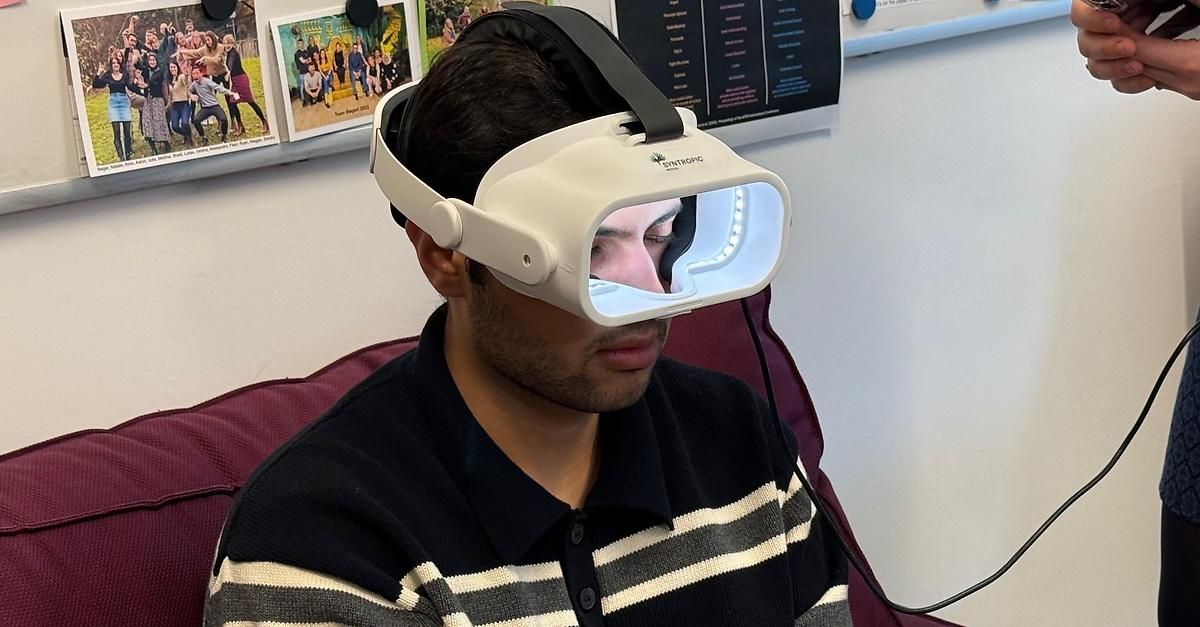 Ein Mann mit einer Syntropic-Virtual-Reality-Brille sitzt auf einem Stuhl, möglicherweise in einem medizinischen oder Forschungsumfeld.