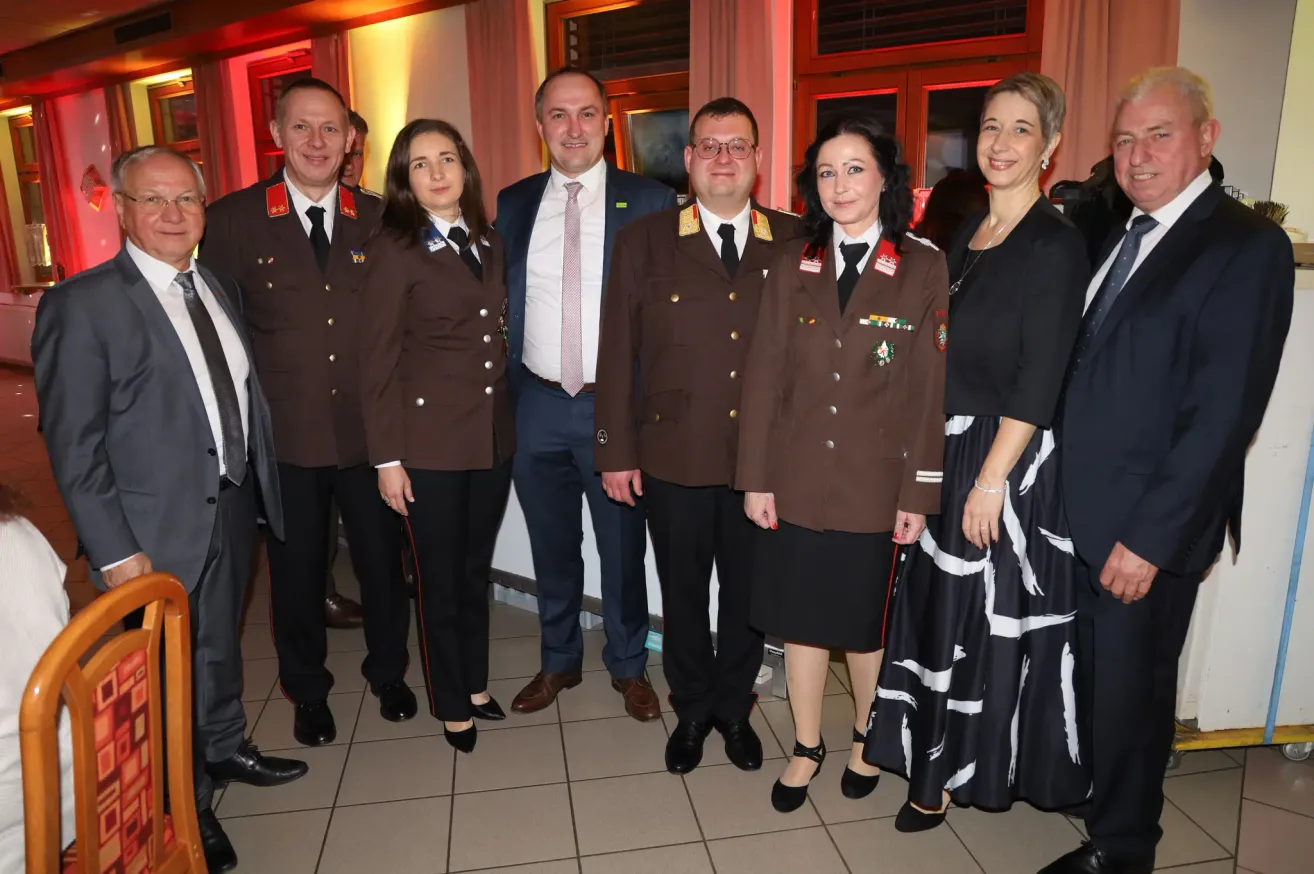 Eine Gruppe uniformierter Personen steht in einem Raum zusammen. Fünf von ihnen tragen militärische Uniformen, während die anderen formelle Kleidung tragen.