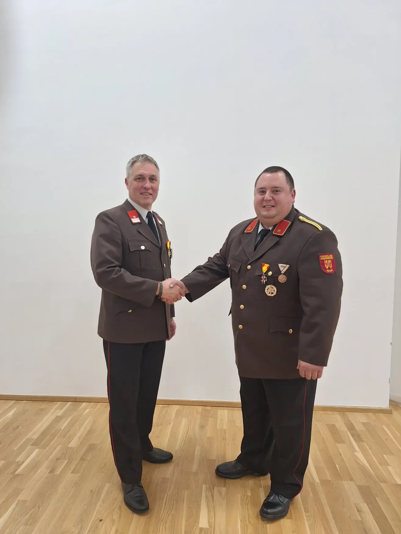 Zwei Männer in Militäruniformen schütteln sich die Hände in einem Raum mit weißer Wand und Holzboden.