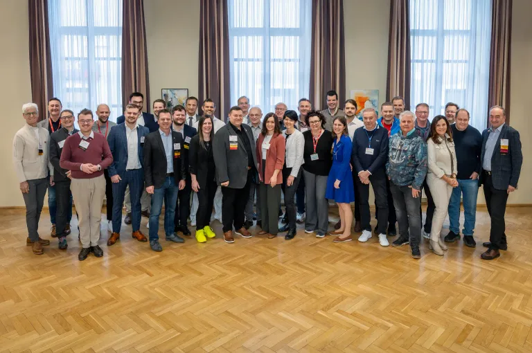 A group of people in formal attire pose for a photo in a room with large windows and wooden floors.